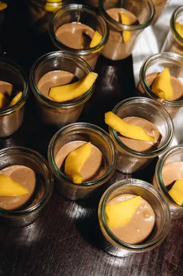 lots of little glasses filled with a chocolate dessert accompanied by cake and mango slices