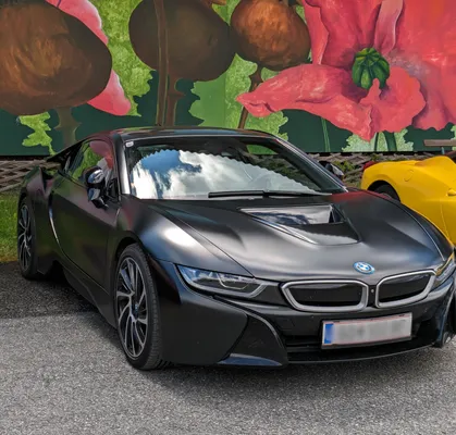 matte black bmw shining beautifully in the sky light with a wall painted with colourful flowers in the background