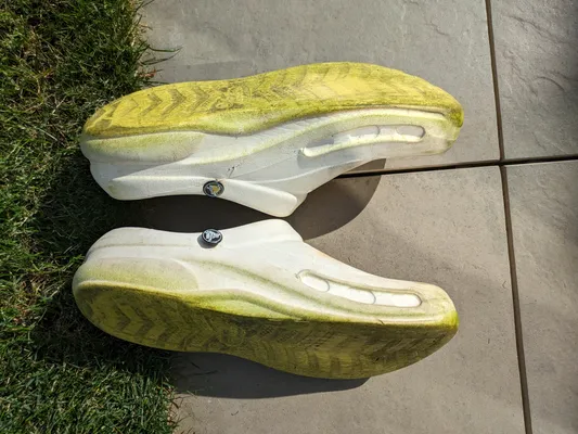 two pairs of gardening shoes with soles completely stained green from the grass